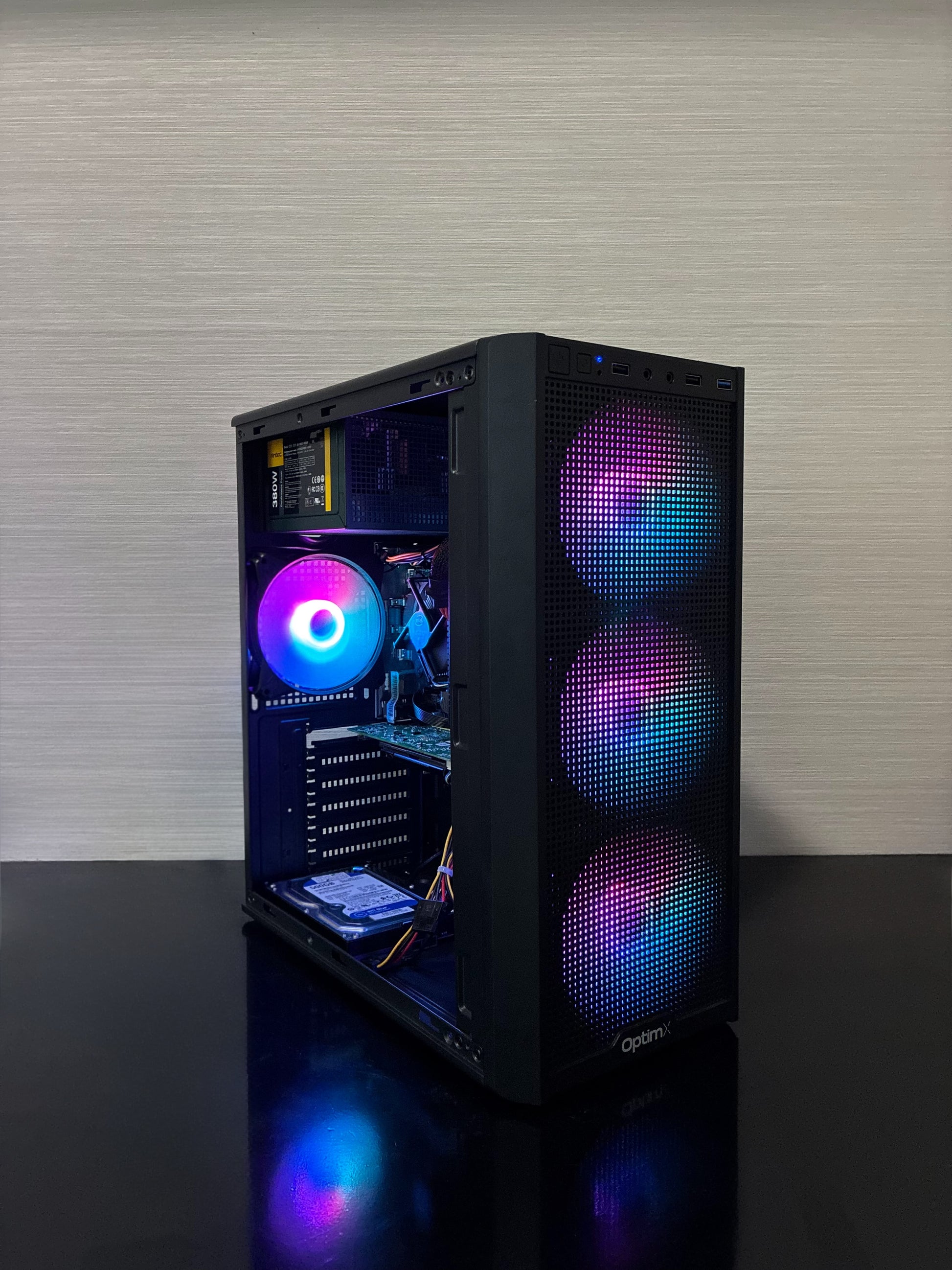 Carcasa de gaming a PC-ului BUENO SUMMER V3 iluminată în timpul funcționării, așezată pe un birou modern, evidențiind designul compact și panoul lateral