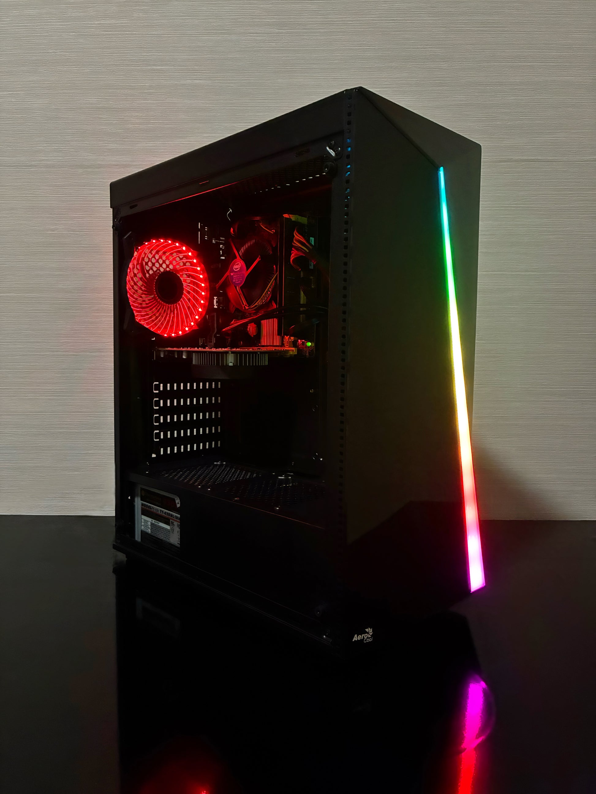 Un sistem PC Gaming BUENO START V2, asamblat într-o carcasă neagră Aerocool RGB. Imaginea prezintă panoul lateral transparent, prin care se văd componentele: procesorul Intel Xeon, placa video NVIDIA GTX 1050 2GB, cei 16GB RAM și stocarea duală (SSD de 256GB și HDD de 500GB). Se observă iluminarea RGB de la ventilatorul Antec din față și ventilatorul spate cu LED Genesis.