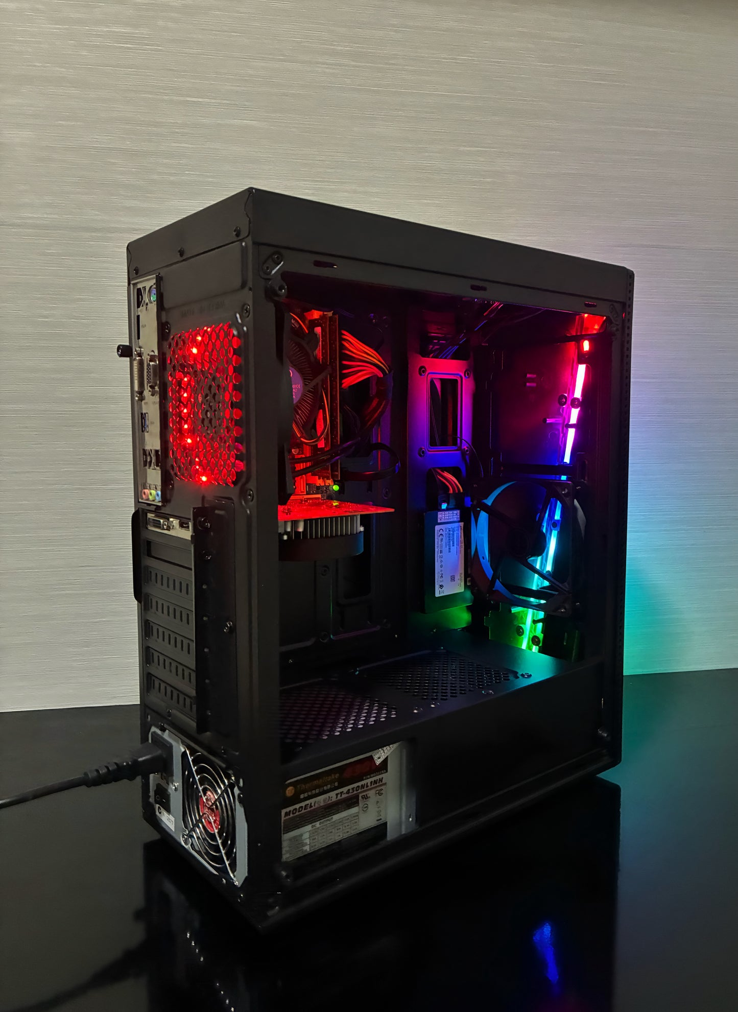 Carcasa neagră Aerocool RGB a PC-ului Gaming BUENO START V2, văzută din față-lateral. Panoul frontal mesh și panoul lateral transparent evidențiază efectele de iluminare ale ventilatorului Antec RGB și ale ventilatorului spate LED Genesis. Carcasa are un design modern, compact, perfect pentru o configurație de gaming de buget.